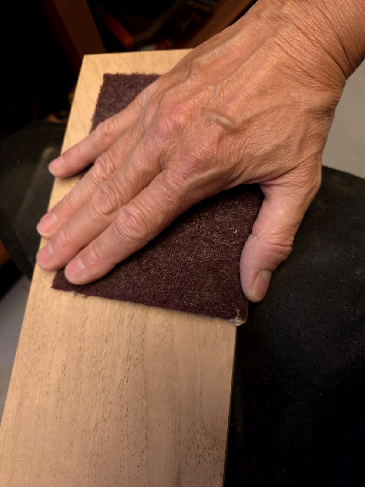 Main ponçant une pièce de noyer européen dans l'atelier Uphile